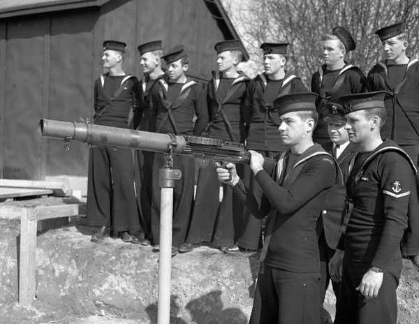 Photographie en noir et blanc – Des marins s’entraînent à manier une mitrailleuse montée sous la supervision d’un instructeur.